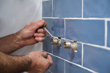 Unrecognizable senior plumber installing water tap with a wrench in bathroom. Installs shower system.