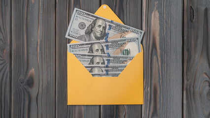 Flat lay of open yellow envelope with hundred dollars banknotes bills on wooden table. Correspondence, money, salary.