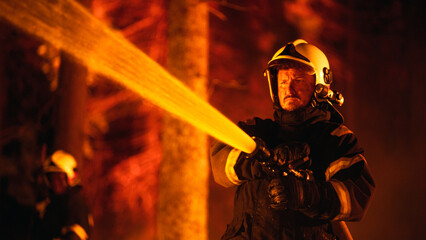 Focused Brave Professional Firefighter Using a Firehose to Fight a Raging Dangerous Forest Fire....