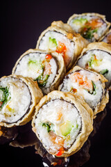 hot sushi roll tempura with salmon cream cheese cucumber avocado unagi on a black mirror background
