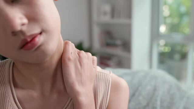Footage of a Young unhappy Asian woman feeling discomfort because of pain in neck and shoulder pain and injury while sitting on the sofa in the living room. Health care and medical concept.