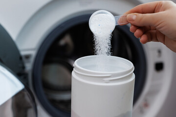 Woman hand pouring washing powder. Measuring cup with granular solid detergent. Open washing machine