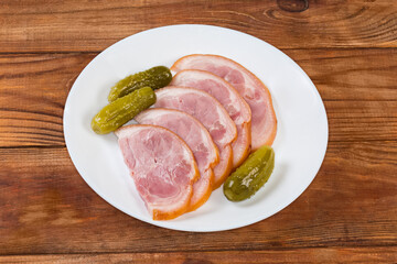 Sliced boiled-smoked pork knuckle and pickled cucumbers on plate