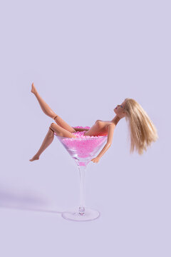 Naked doll bathing in a martini glass full of pink balls. Creative summer concept of minimal beauty.