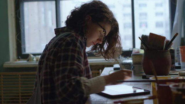 Designer Using Tablet Computer. 30s woman drawing on tablet sitting at the desk by the window.