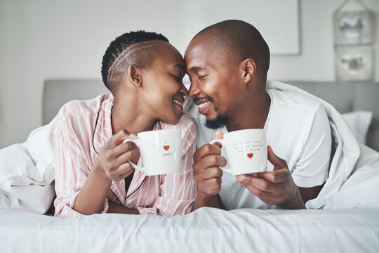 Love, Valentines Day And Black Couple Gift Cups Lying In Bed In The Morning Drinking Coffee In The Bedroom Together. Kiss, Romantic And Happy Lovers Relax In A Home, House Or Apartment On Holiday