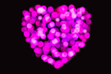 Magenta colour confetti of light highly defocused in the shape of a heart on a black background...