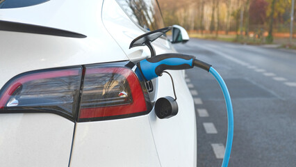 Electric vehicle charging at a public charging station in a city setting. New energy vehicles, eco-friendly alternative energy for cars. Electric cars are becoming more common and gaining popularity.