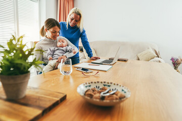 Women gay couple holding her infant son at home - Smart working and family concept - Focus on right mother face