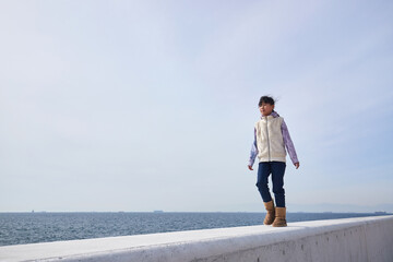 冬の海の海岸の堤防で散歩して遊んでいる小学生の女の子の様子