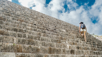 tourist woman with a hat climbing stairs of the maya pyramids  at Uxmal, in Yucatan, Mexico