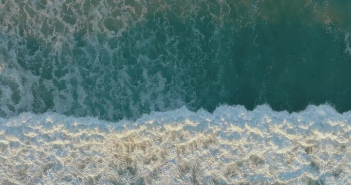 Aerial view of drone flying above beautiful beach with views of ocean waves and water crashing on to sandy beach. Aerial view looking straight down onto crashing waves. Foamy ocean waves. 4k. Drone. 