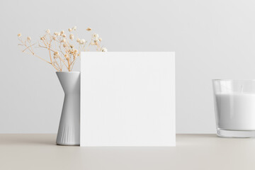 Square invitation card mockup with a gypsophila decoration on the beige table.