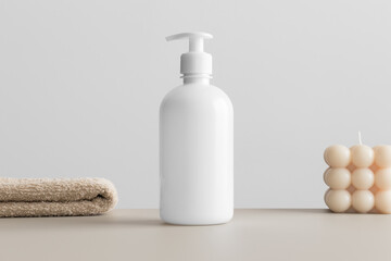 White cosmetic liquid soap dispenser bottle mockup with a candle and a towel on the beige table.