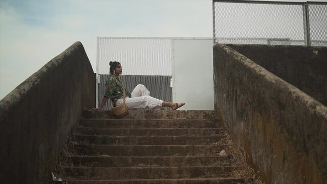 Long shot of a girl sitting on a concrete staircase. Posing for a photo. Serious Indian Girl. One person.