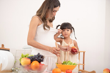 Mom with her two children eating fruits and vegetables. Mother with daughter having breakfast at home. Happy lifestyle family. Mother with her children in the kitchen cooking together.