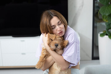 Young and beautiful woman sitting on the couch and hugging her adorable pet dog. Perfect friendship concept	