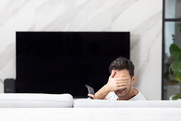 Obraz premium Stressed man sitting on the couch and watching tv. Empty screen for collage concept