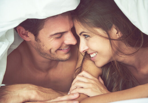 Couple, happy and love in bed, waking up and bonding in a bedroom together, flirting and romantic. Romance, man and woman relax, intimate and resting at hotel for valentines day, anniversary or bond
