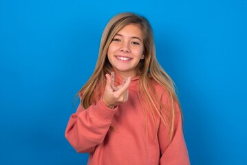 caucasian teenager girl wearing pink sweater over blue background holding an invisible aligner...