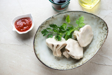 Oval bowl with georgian traditional khinkali dumplings, horizontal shot on a beige stone background, elevated view