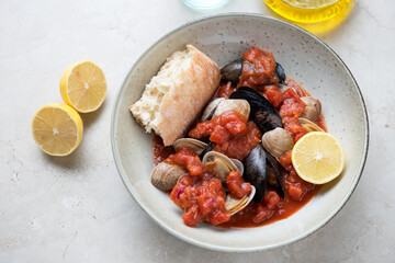Plate with mussels and vongole in thick tomato broth, horizontal shot on a light-beige stone background, selective focus