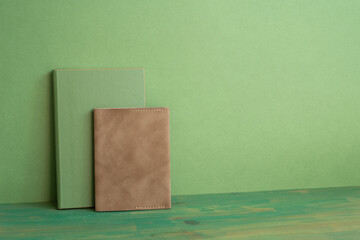 Green and brown diary notebook on wooden desk. green wall background. workspace, copy space