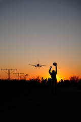 A backlit woman raises her arms to airplanes at sunset as a sign of travel and adventure.