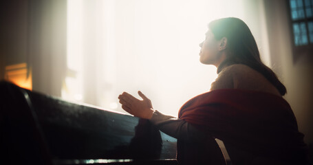 Young Christian Woman Sits Piously in Majestic Church, with Folded Hands She Seeks Guidance From Faith and Spirituality while Praying. Religious Belief in Power and Love of God. Side View - obrazy, fototapety, plakaty
