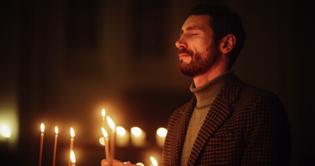 Aesthetic Shot of Young Christian Man Lighting a Candle in Church, Praying and Expressing Devotion...