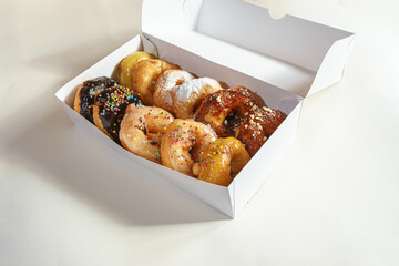 Different donuts in a white cardboard box on a light background