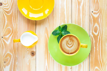 cup of cappuccino coffee on  light green plate and yellow milk jug .on wooden table, top view - 569162865