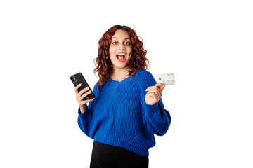 Happy woman standing isolated over white background holding a credit card and a phone looks overjoyed and looks at the camera. Seeing an incredible campaign or discount ad. Wants to shop immediately.