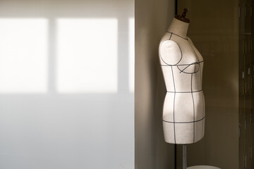 Empty tailor's textile female mannequin with black lines with sunlight on it for dressmaker working...