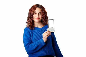 Naklejka premium Happy woman wearing blue knitted sweater standing isolated over white background holds phone and credit card together, shows them to the camera and poses looking at the camera, smiling.