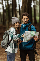 Smiling young european people tourists in jackets with backpack walk in autumn forest, look at map