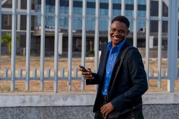 young handsome African business man standing using his phone smiling, looking at the camera