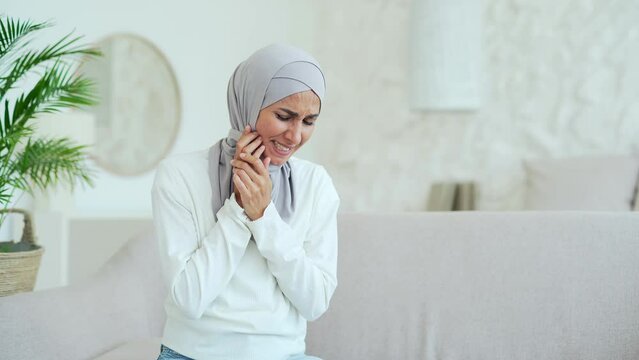 Stressed young Muslim woman in hijab with severe toothache dental pain ache at home alone Sad female suffering from discomfort because caries gum disease or sensitive teeth indoors