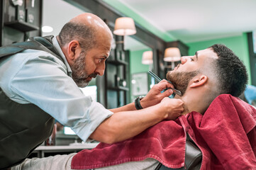 Fototapeta premium Barber using blade shaving razor on client