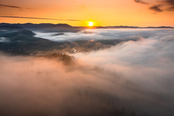 Obraz premium Foggy sunrise over the beautiful Paltinu village from Suceava, landmark of Bucovina region in Romania. Hills and haystacks sunrise landscape.