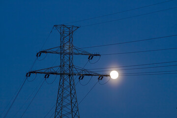 View of a high voltage line pylon, dark sky and moon in the background, symbolic image of power...