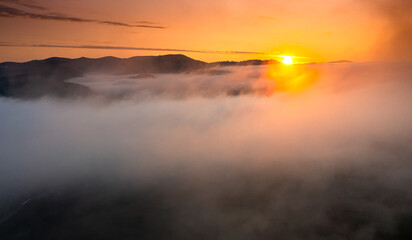Amazing foggy sunrise landscape. Aerial view with clouds over a forest in beautiful warm light. Landscapes of Romania.