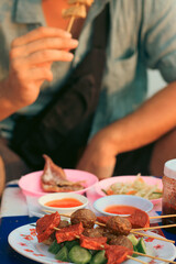 A tourist eating one of the skewers from a plate full of different khmer street food skewers or...