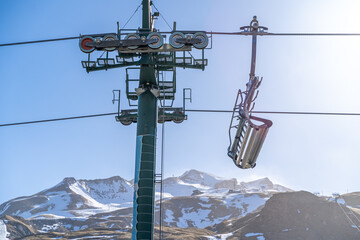 Chair lift in a ski resort during a sunny winter day with snow capped mountains