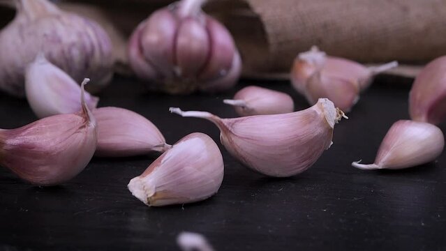 Fresh garlic clove falling on black background. The raw garlic is one of the most popular ingredients of the basic recipes with nutritional properties, infamous aroma and health benefits. Slow motion