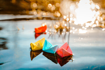 Multicolored paper boats. Colorful pink yellow blue orange ships in big spring snow puddle on winter street. Warm wet rainy weather, old grass. Hello spring, autumn. Children play, have fun outdoors