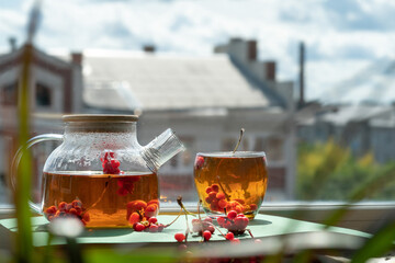 Tea with berries in a glass teapot on a window