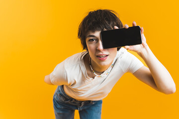 Advertising concept. Young Gen Z girl covering her face with smartphone with black screen. Orange yellow background horizontal studio shot. High quality photo © PoppyPix