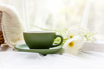 Fototapeta na wymiar Coffee morning. Green steaming cup of hot coffee for relax after working hobbies crochet on white wooden near window with flowers on autumn and winter season. Lifestyle Concept