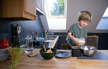The boy prepares the dough from eggs, sugar, sour cream and flour by himself in the kitchen